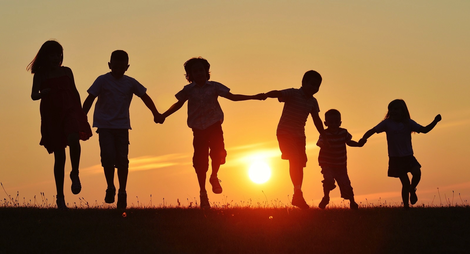 Happy children silhouettes on summer meadow running and jumping